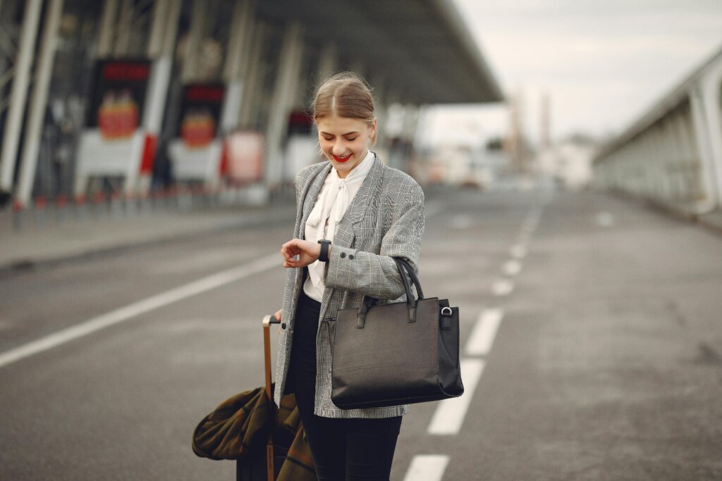 Professional woman with luggage at outdoor airport terminal checking time on wristwatch.